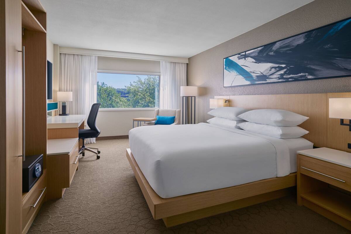 A hotel room with a large bed, a desk with a chair, a TV, and a window with curtains.