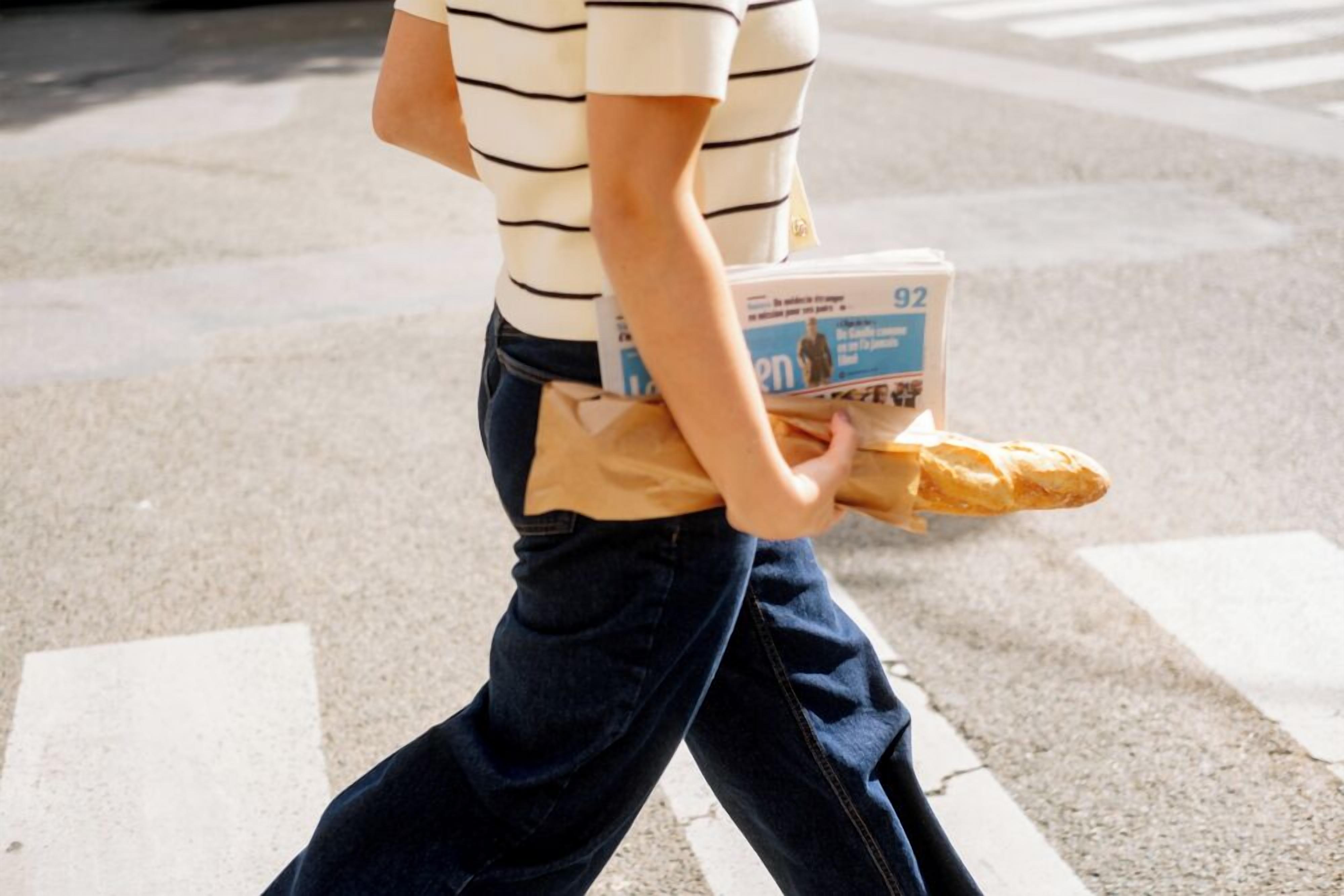 Una persona lleva una baguette y un periódico.