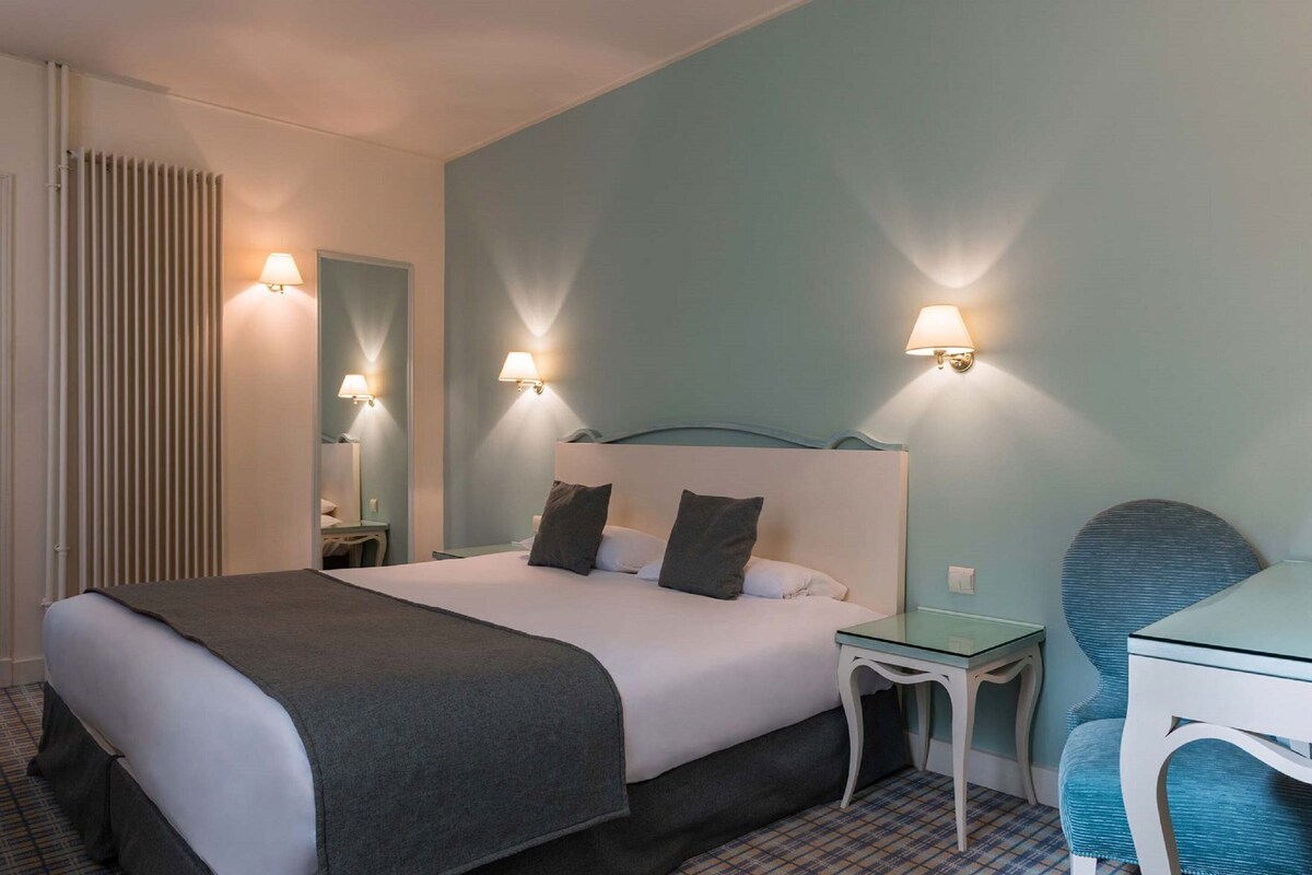 A hotel room with a bed, bedside tables, a desk, and wall-mounted lamps.