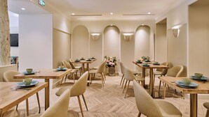 A dining area with wooden tables and chairs, a herringbone floor pattern, and wall-mounted lighting.