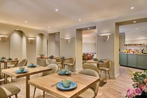 A modern dining area with wooden tables and chairs, a kitchen area with cabinets and appliances, and a decorative wall with a floral arrangement.