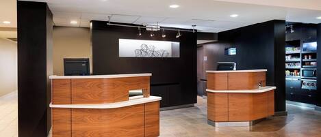 A reception area with wooden reception desks, a digital display, and a wall-mounted artwork.