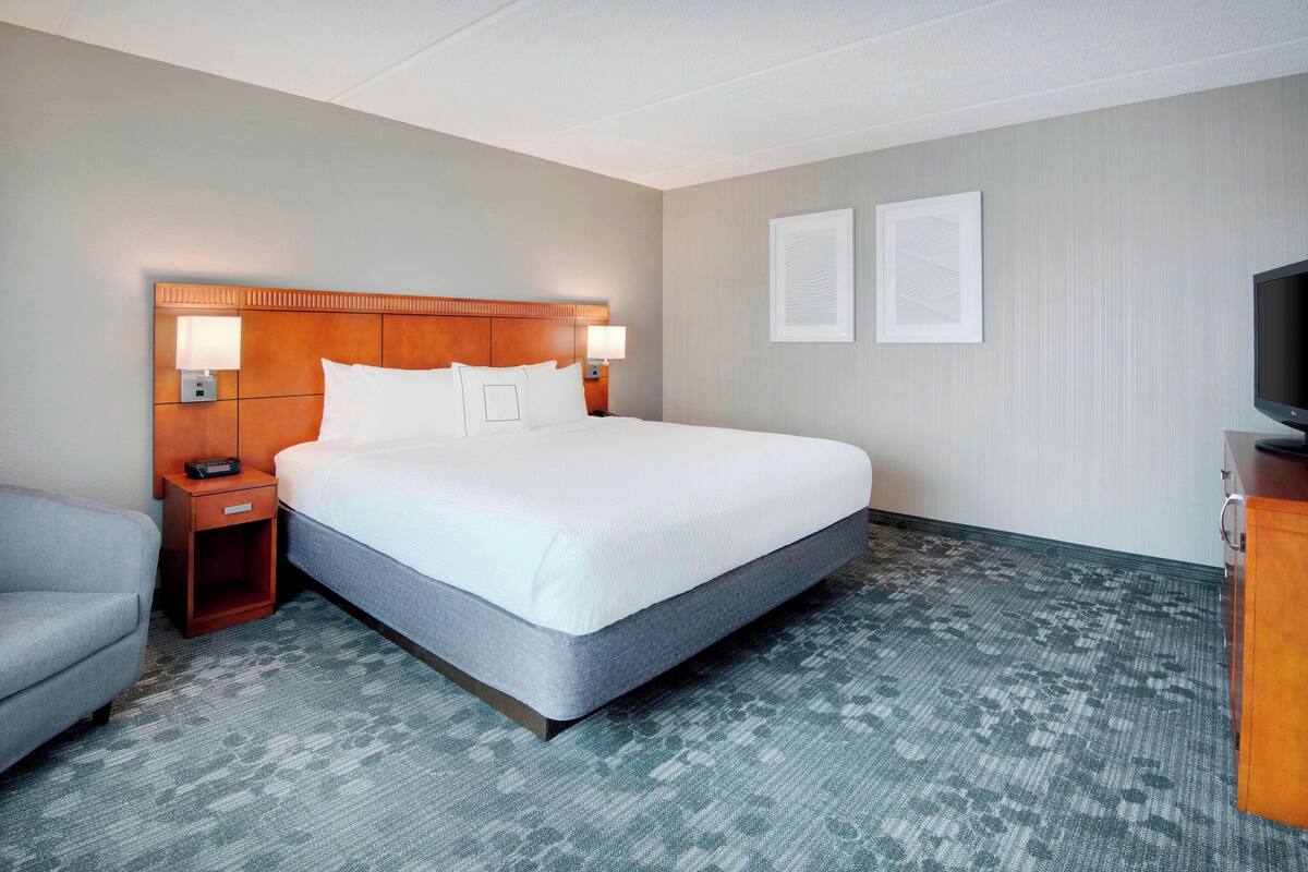 A hotel room with a large bed, two bedside lamps, a TV, a desk, and a chair.