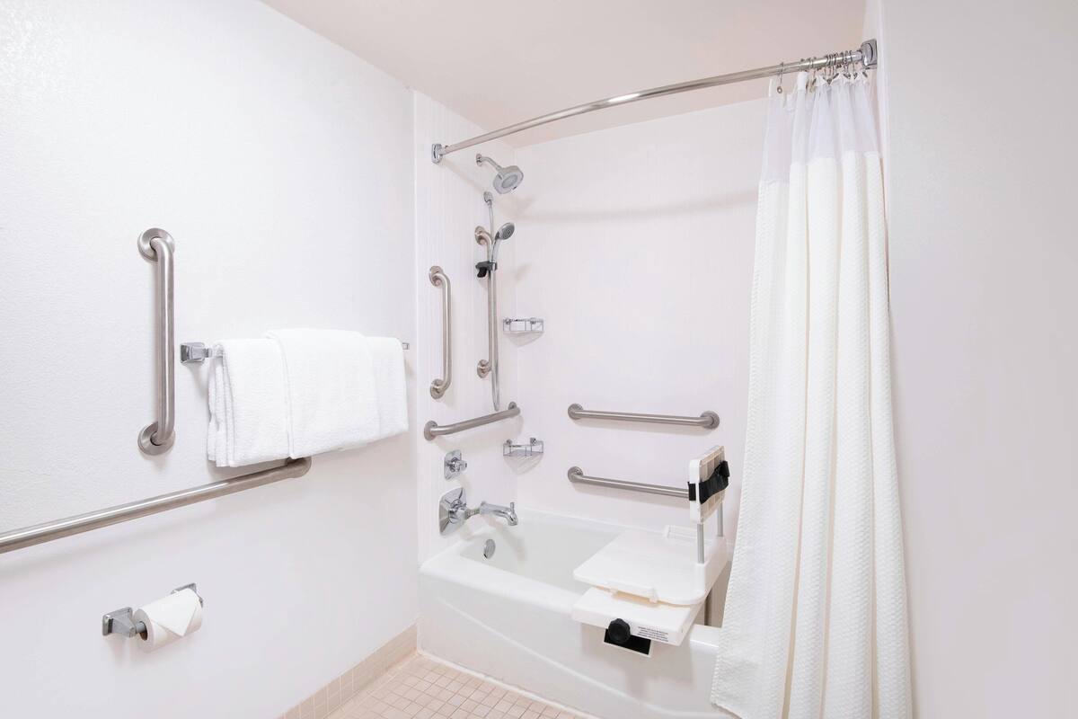 A bathroom with a bathtub, grab bars, a towel rack, and a toilet paper holder.