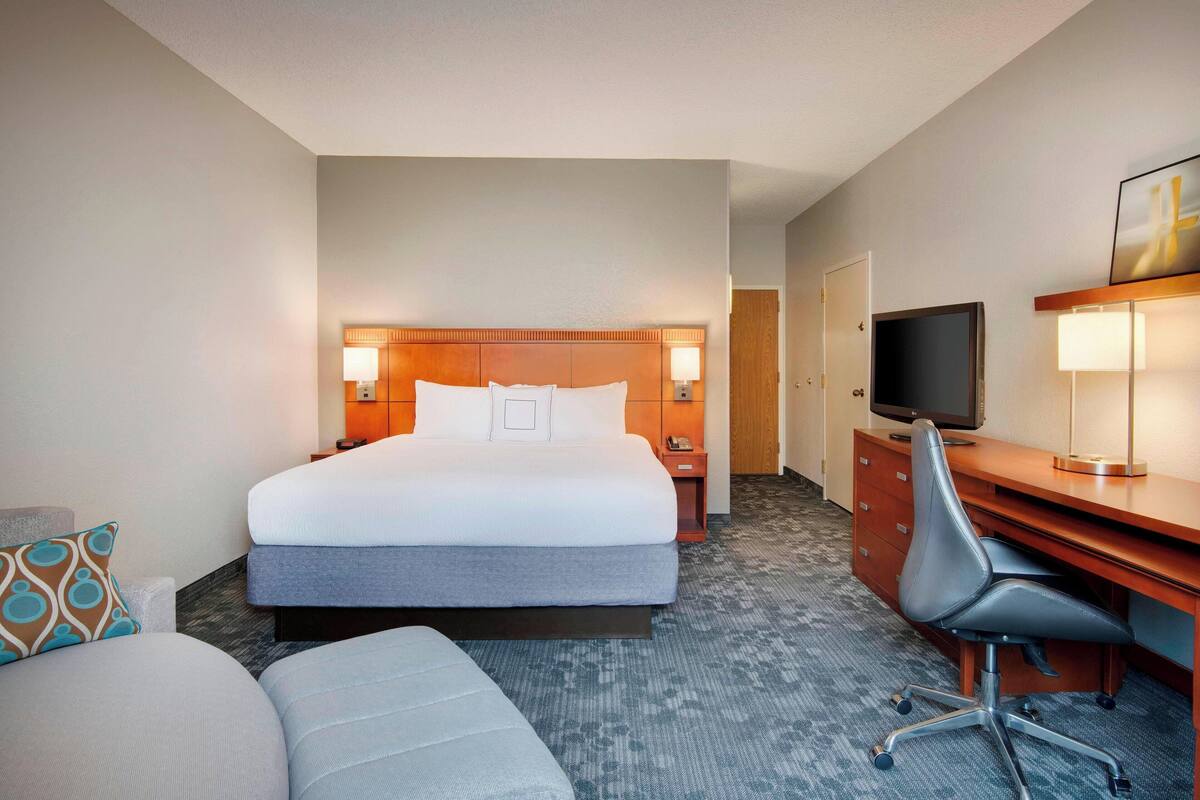 A hotel room with a large bed, a desk with a chair, a television, and a lamp.