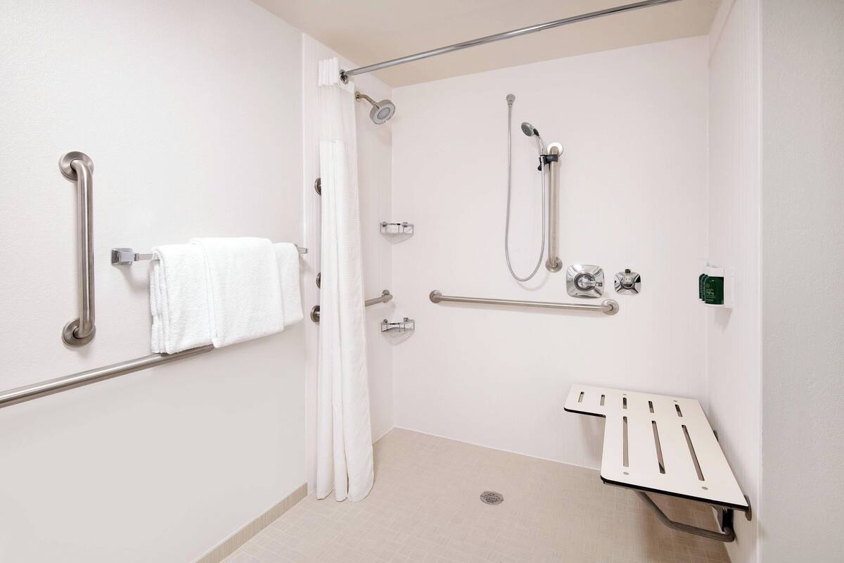 A bathroom with a shower, grab bars, a towel rack, and a bench.