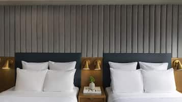 Une chambre d’hôtel avec deux lits, chacun doté de draps blancs et d’une tête de lit sombre. On y trouve deux tables de chevet avec des lampes, et une petite plante est posée sur l’une d’elles.