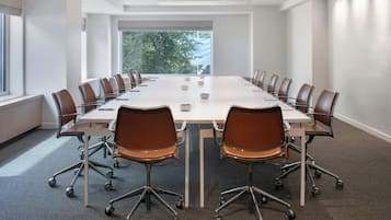 A conference room with a long table, chairs, and a view of trees through the windows.