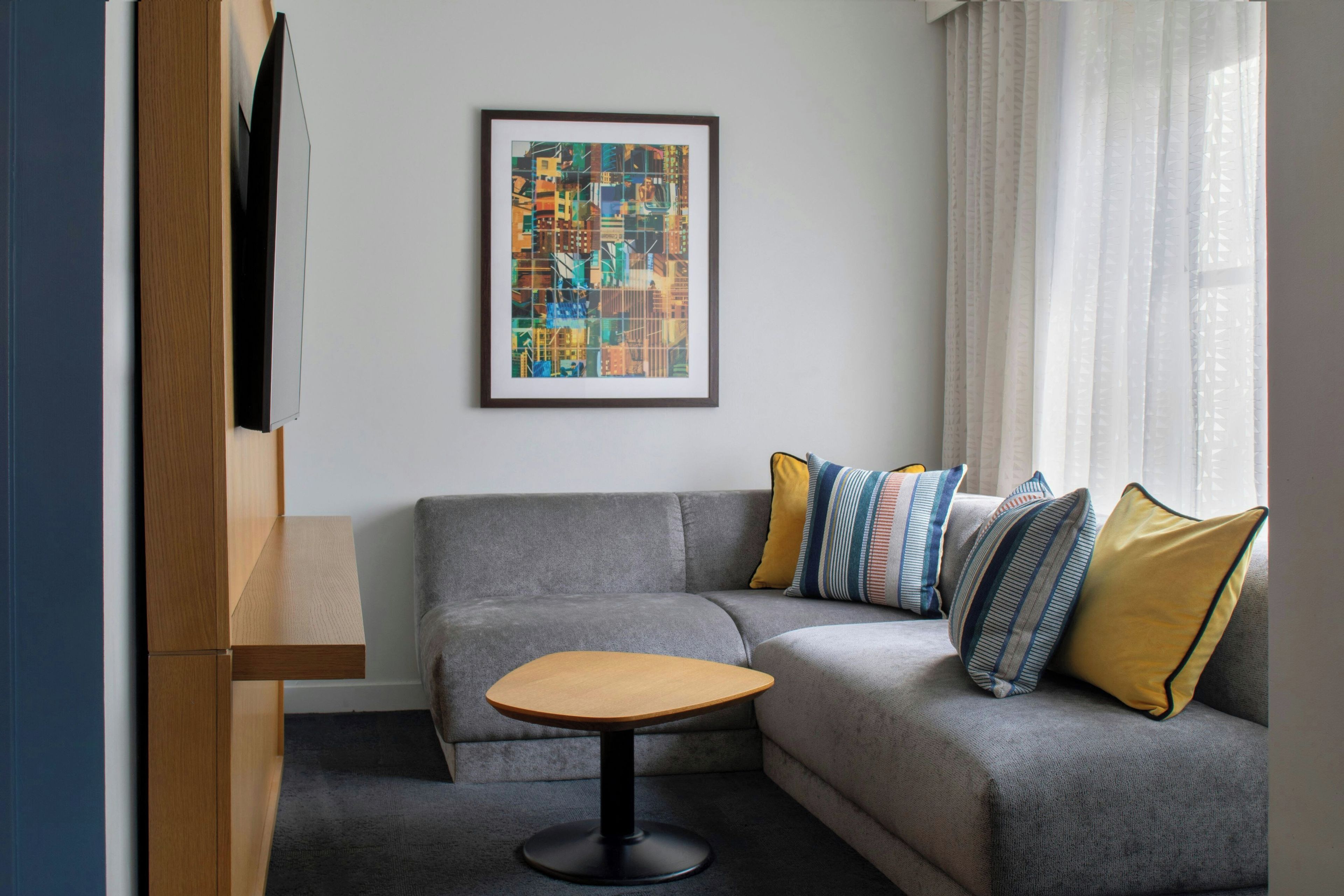 A modern living room with a grey sofa, a small wooden table, and a colorful abstract painting on the wall.