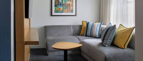 A modern living room with a grey sofa, a small wooden table, and a colorful abstract painting on the wall.