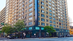 A tall, multi-story building with a prominent vertical feature, likely a lobby or atrium, and a ground-level entrance with a green awning.