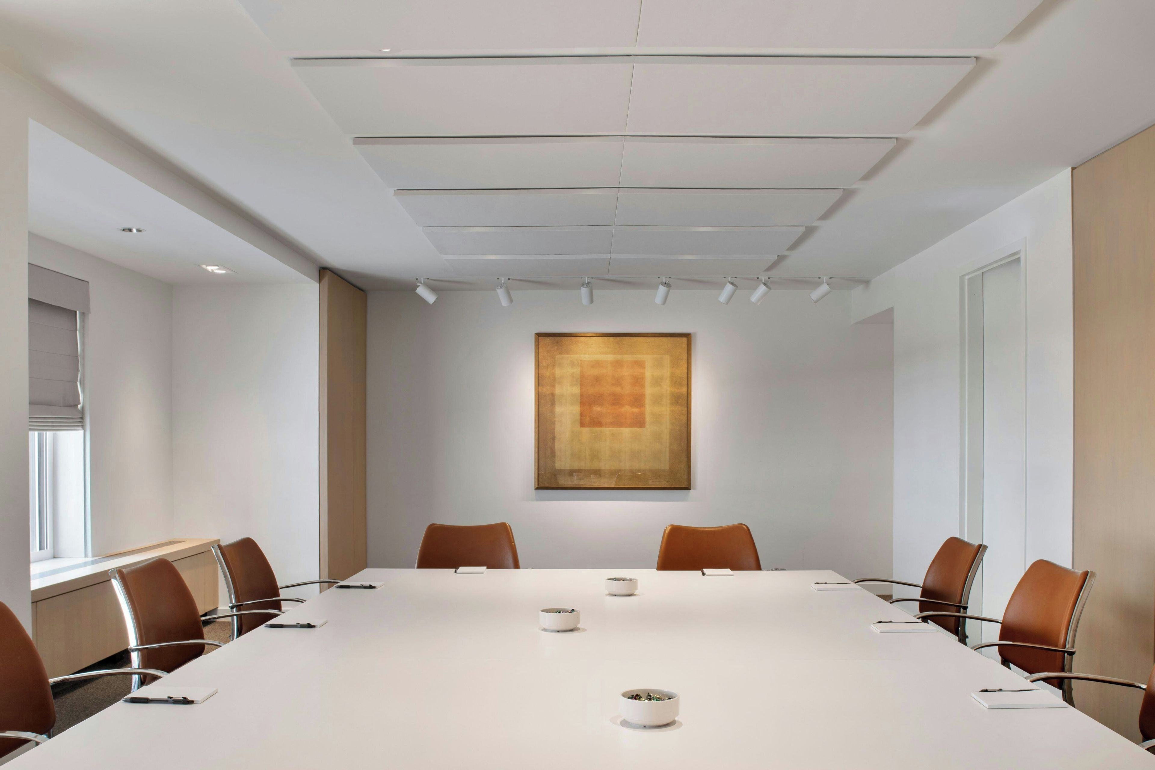 Un salón de conferencias con una larga mesa, sillas, un cuadro en la pared y luces en el techo.