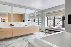 A modern bathroom with a large mirror, marble countertop, and a bathtub.