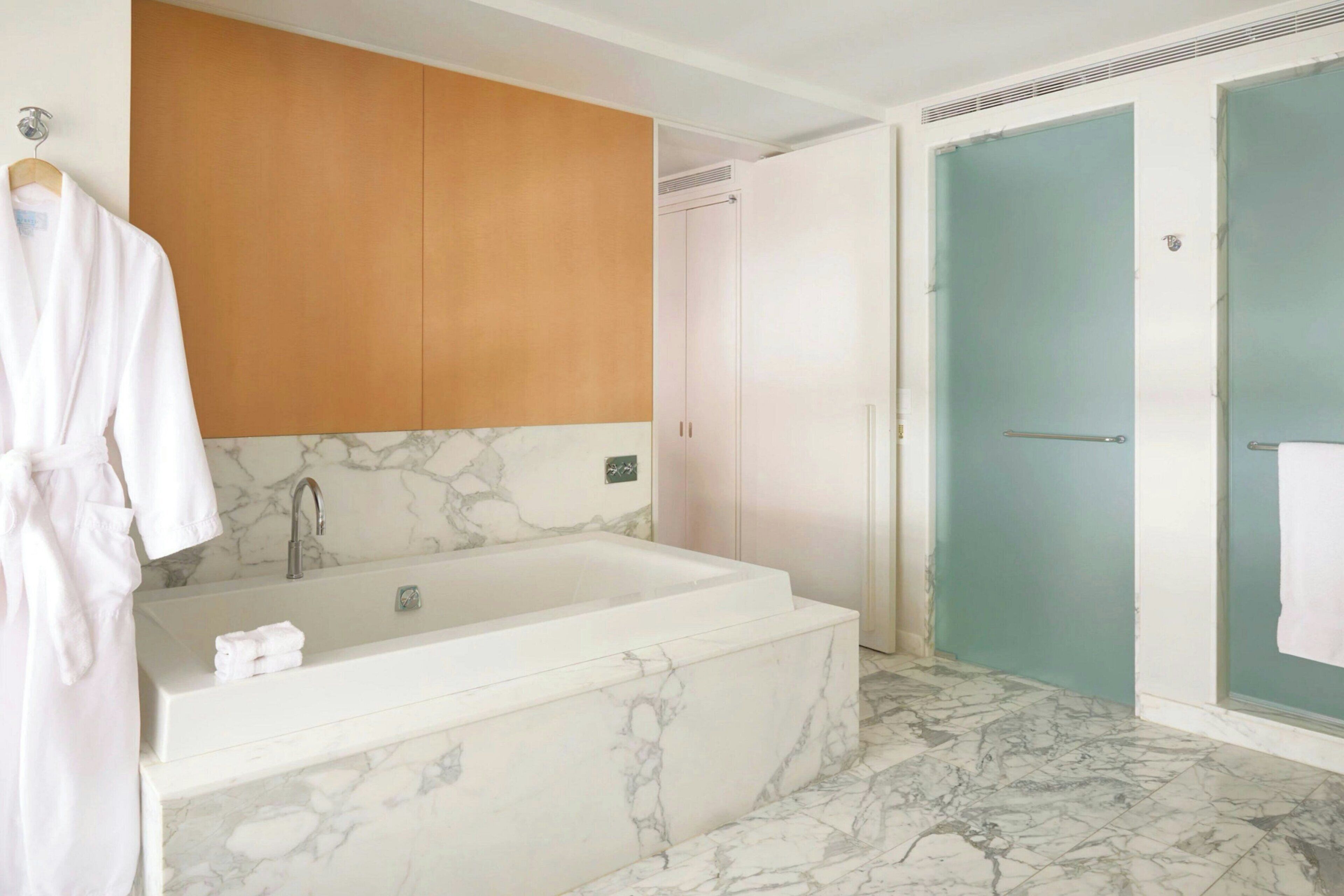 Un baño con una bañera de mármol, un armario de madera y una puerta color turquesa.