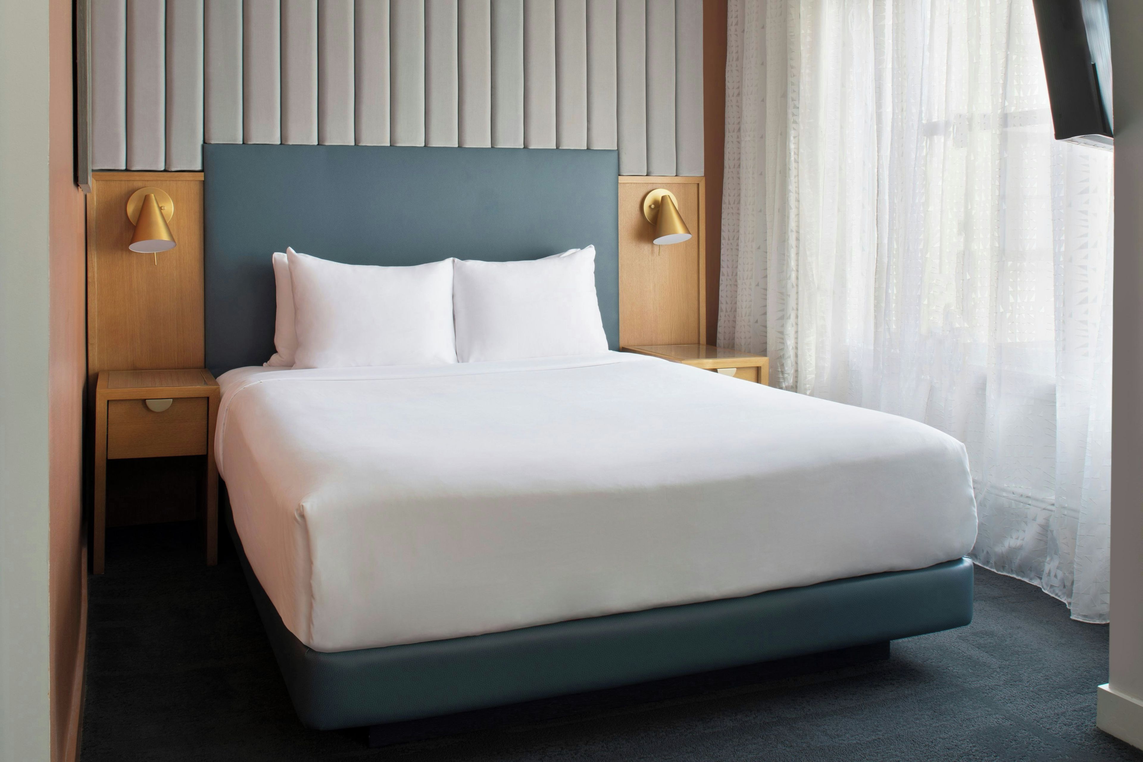 Une chambre d’hôtel avec un grand lit, deux tables de chevet et une tête de lit dotée de lattes verticales.