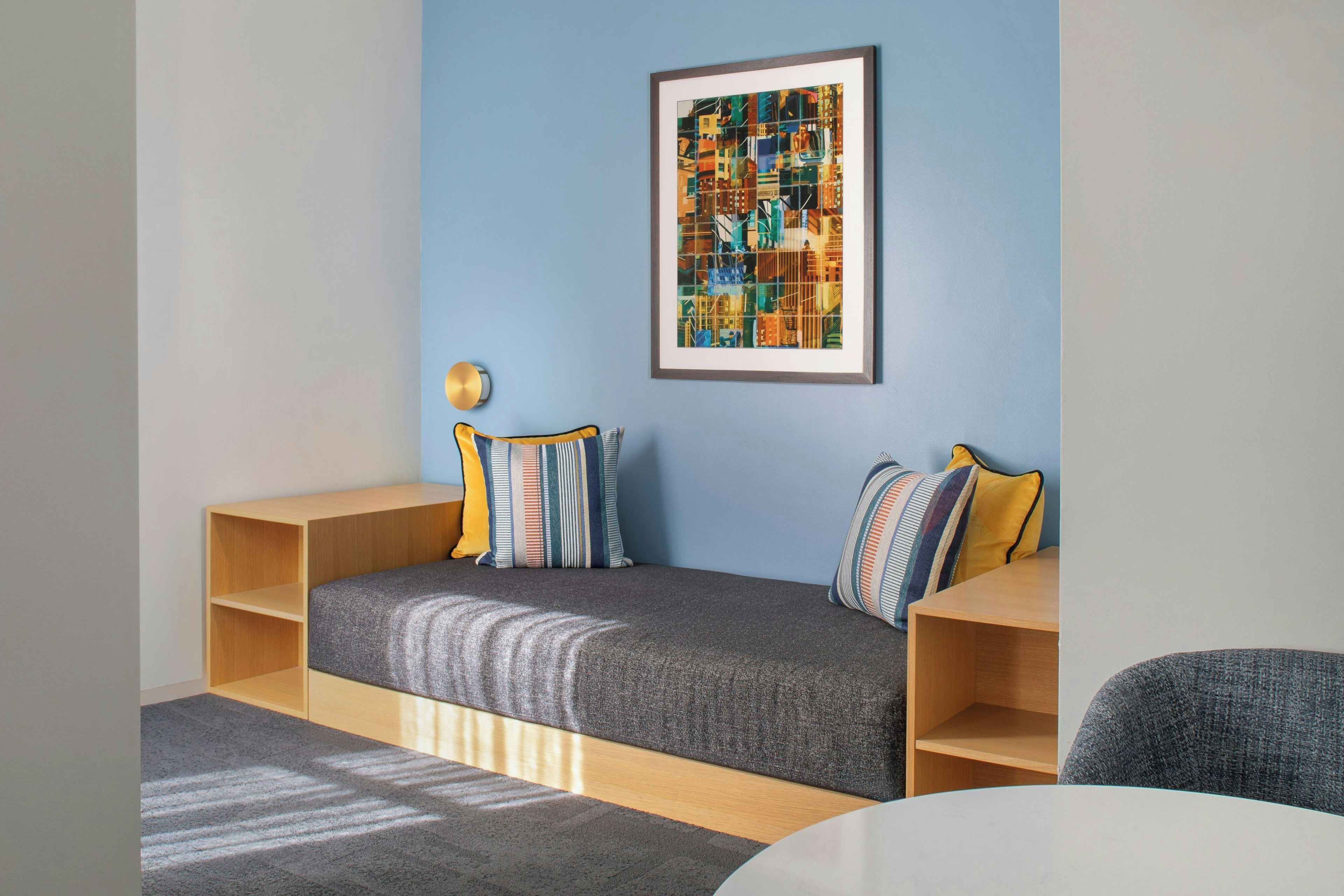 Una habitación moderna con una cama empotrada, un cuadro abstracto enmarco y una pequeña mesa.