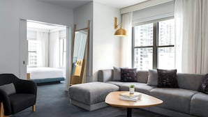 A modern living room with a grey sofa, a black armchair, a round coffee table with a book and a plant, and a large window with curtains.
