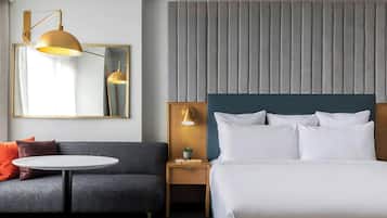 A hotel room with a bed, a bedside table with a lamp, a round table, a sofa, and a large mirror.