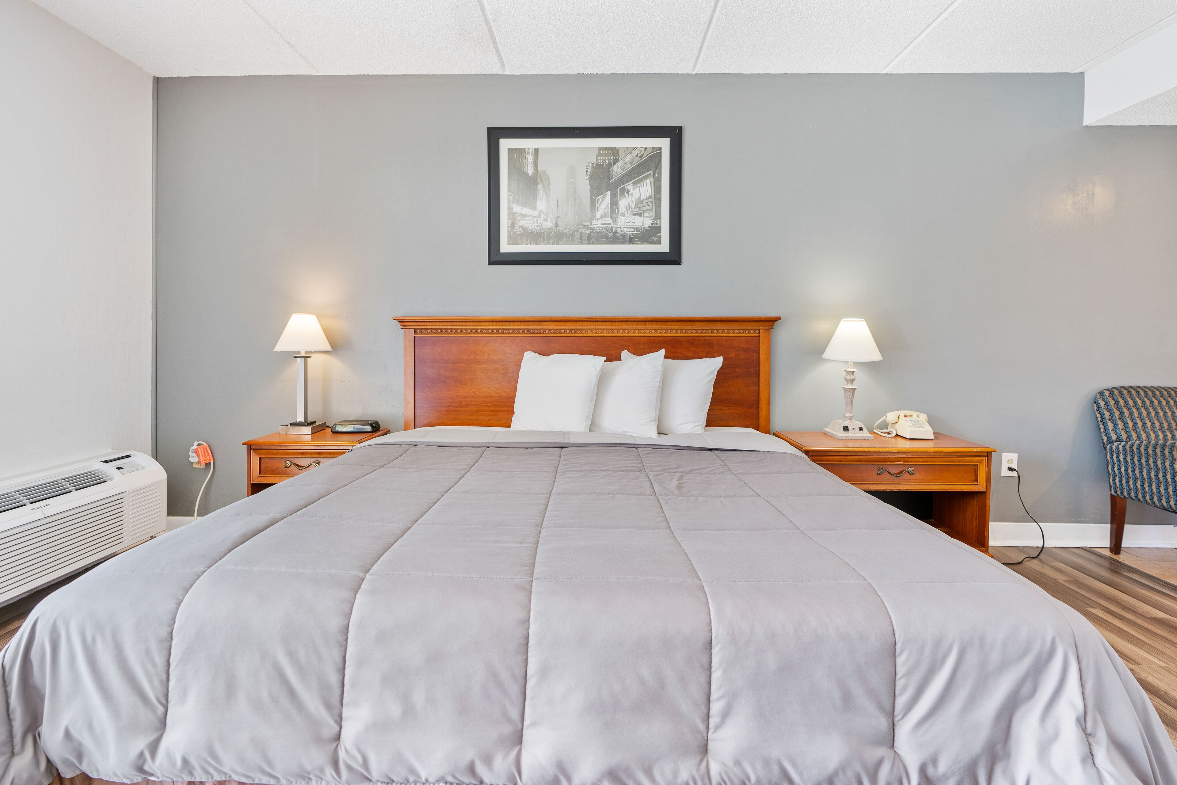 A hotel room with a large bed, two bedside tables with lamps, a framed picture on the wall, and a chair.