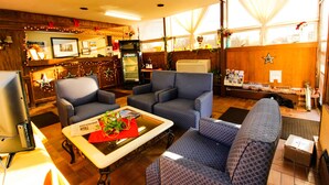 A cozy living room with blue patterned sofas, a coffee table with a red vase, and a television. - FairBridge Inn & Suites at West Point (Highland Falls)