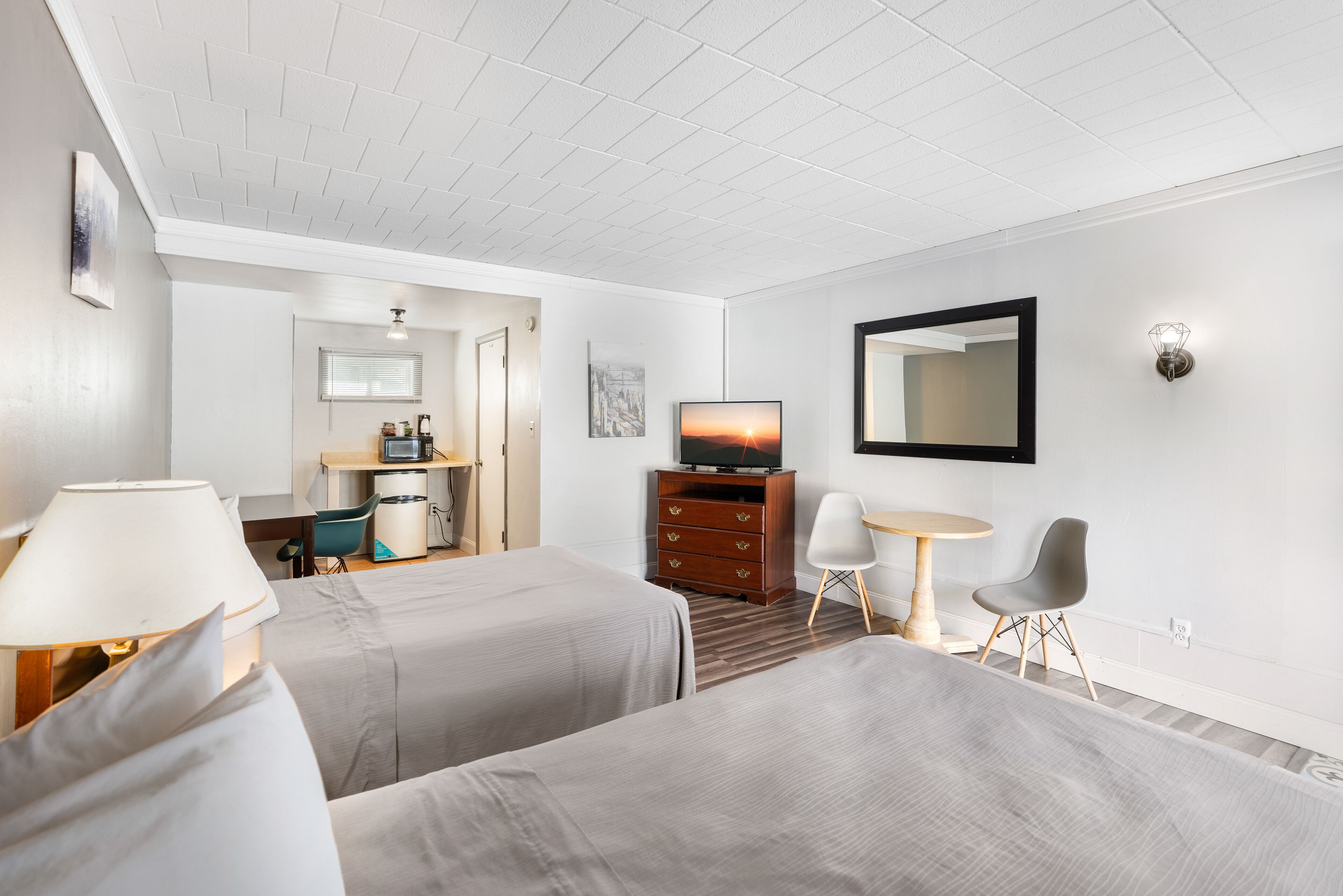 Hotellihuone, jossa on kaksi sänkyä, työpöytä tuolilla, televisio, peili ja lamppu.