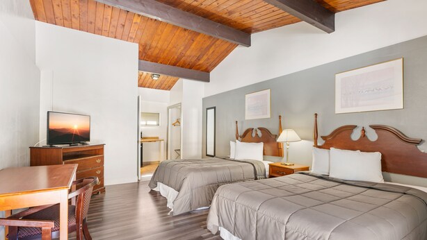 A hotel room with two beds, a wooden desk, a television, and a dining area. - FairBridge Inn & Suites at West Point (Highland Falls)