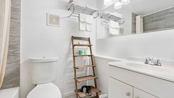 A modern bathroom with a toilet, a wooden shelf, a sink, and a mirror.