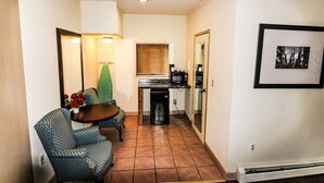 A compact living space with a kitchenette, a dining area with patterned chairs, and a small table. - FairBridge Inn & Suites at West Point (Highland Falls)