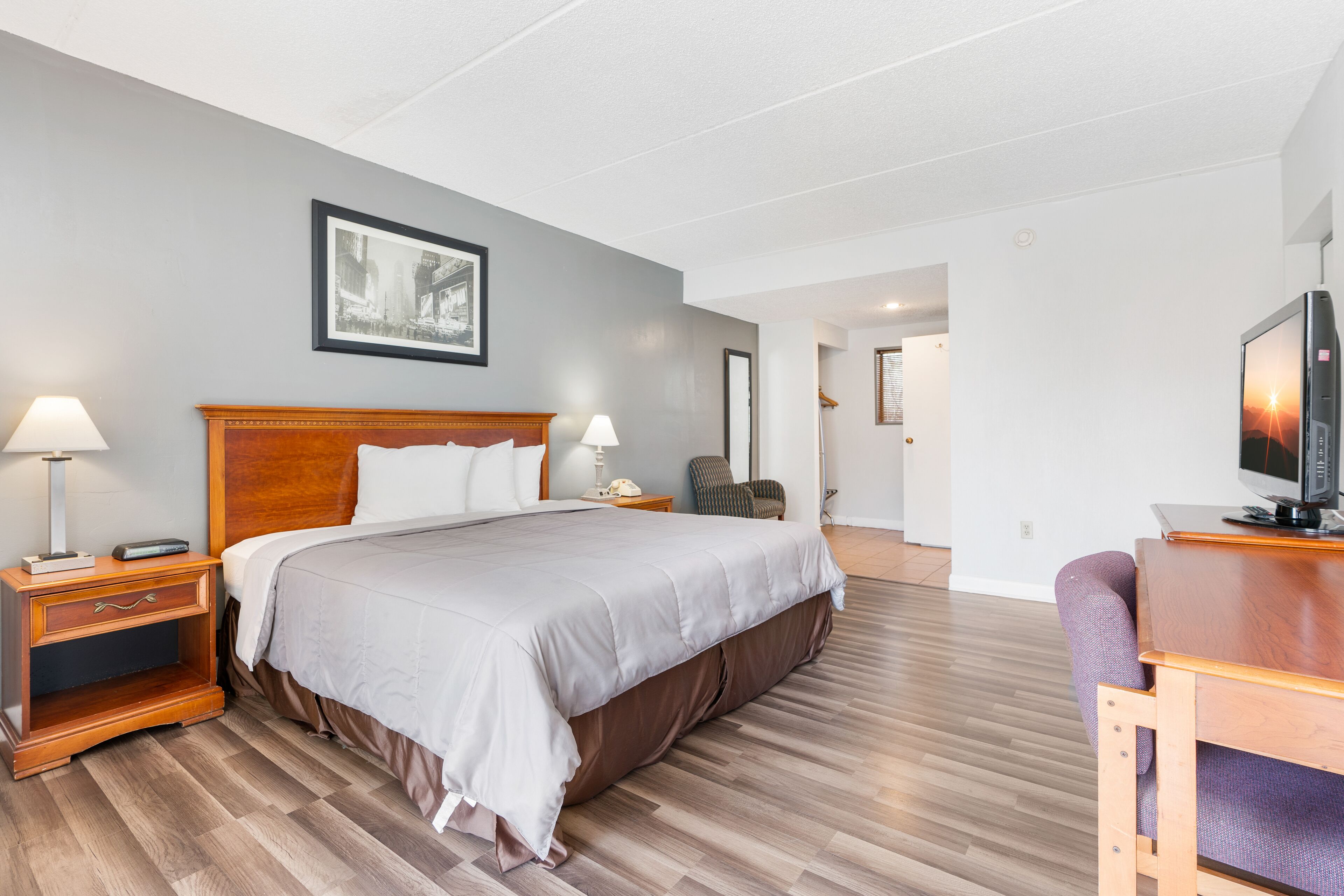 Une chambre d’hôtel avec un grand lit, des tables de chevet en bois, un bureau avec une télévision et un tableau encadré au mur.