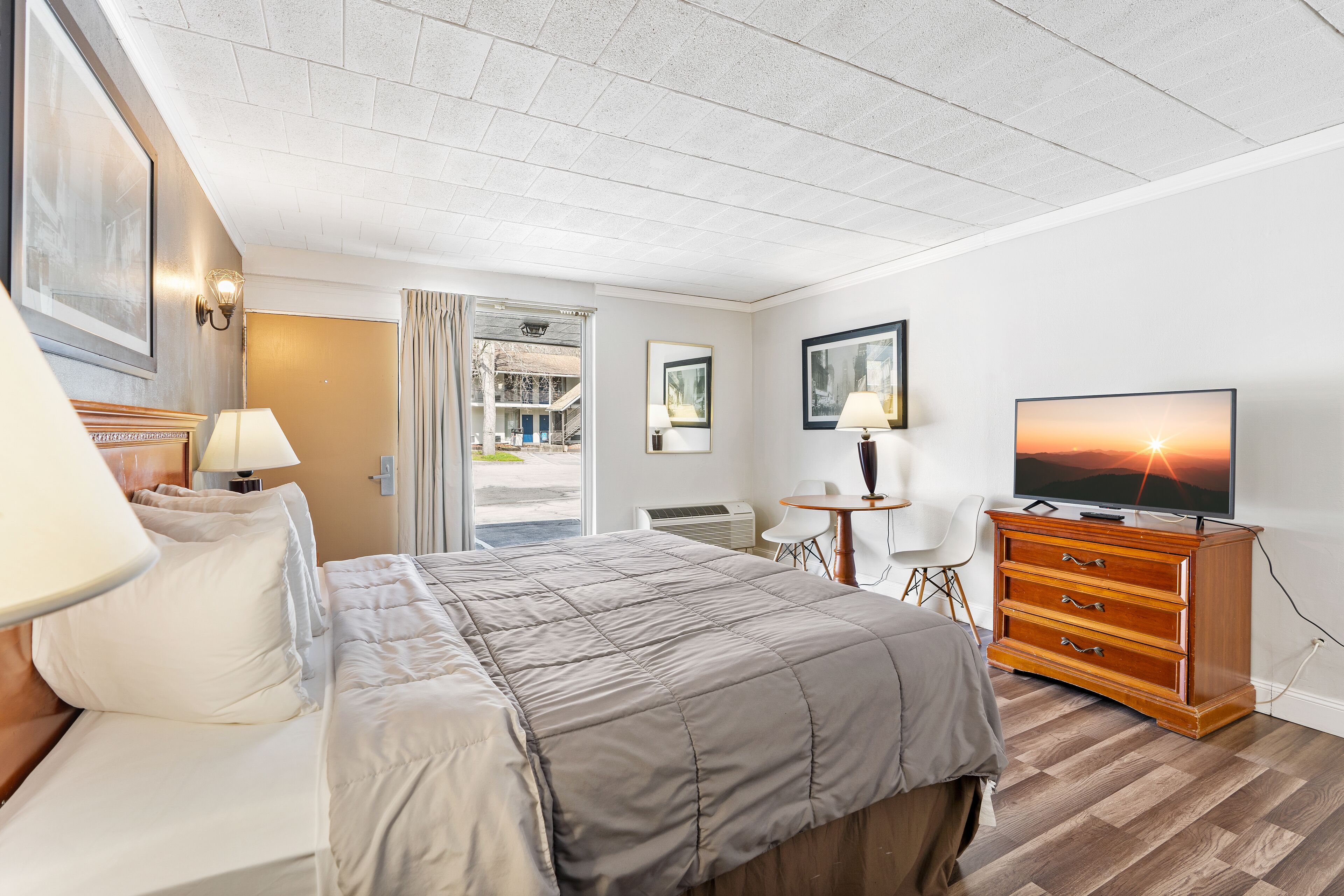 A hotel room with a bed, a wooden dresser, a television, and a desk with a chair.