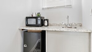 A compact kitchenette with a microwave, a small sink, and a window with blinds. - FairBridge Inn & Suites at West Point (Highland Falls)