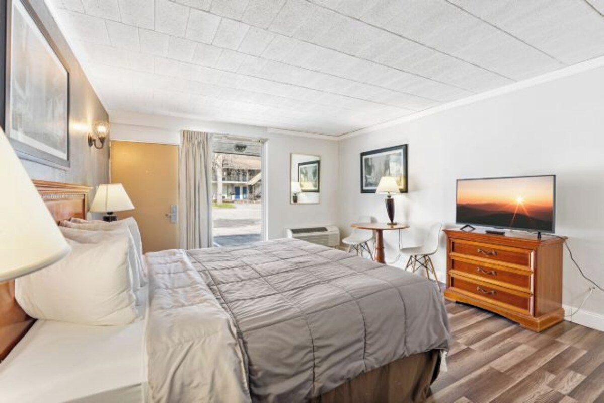 A hotel room with a bed, a dresser, a TV, and a desk with a chair.