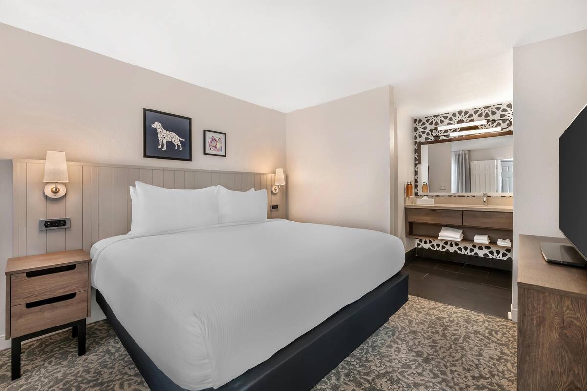 Une chambre d’hôtel avec un grand lit, des tables de chevet, un miroir et un téléviseur.
