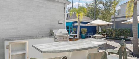 Cocina exterior con parrilla, asientos de bar y zona junto a la piscina.