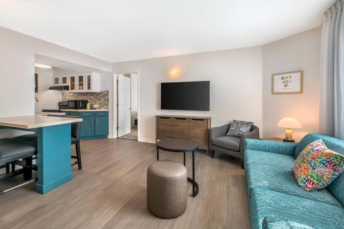 Un salon moderne avec un canapé de couleur turquoise, un pouf rond et un téléviseur à écran plat fixé au mur.
