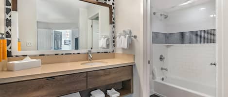 A modern bathroom with a large mirror, a sink, a vanity with drawers, a shower area, and a tiled floor.