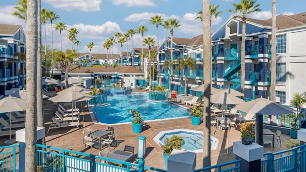 A hotel with a swimming pool, palm trees, and outdoor seating areas.
