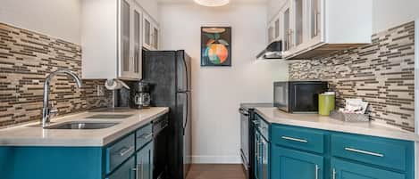 Una cocina compacta con armarios verde azulado, un refrigerador negro y un microondas.