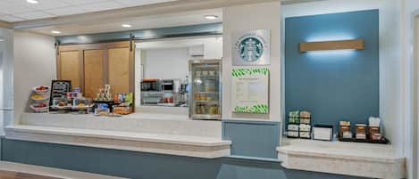 A clean, modern reception area with a counter, seating area, and a wall-mounted Starbucks sign.