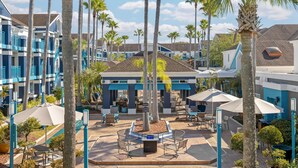 A resort with multiple-story buildings, outdoor seating areas, palm trees, and a central courtyard.