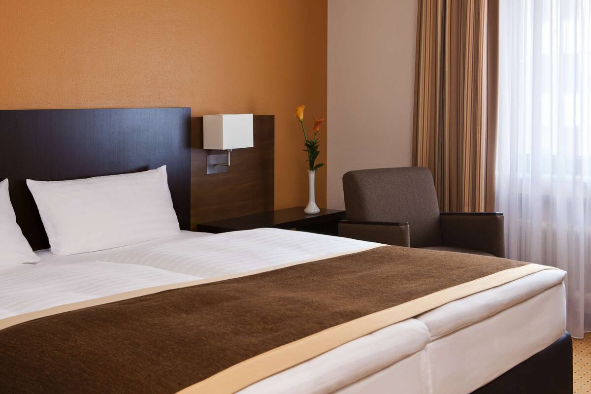A hotel room with a large bed, a nightstand with a lamp, a chair, and a vase with flowers.