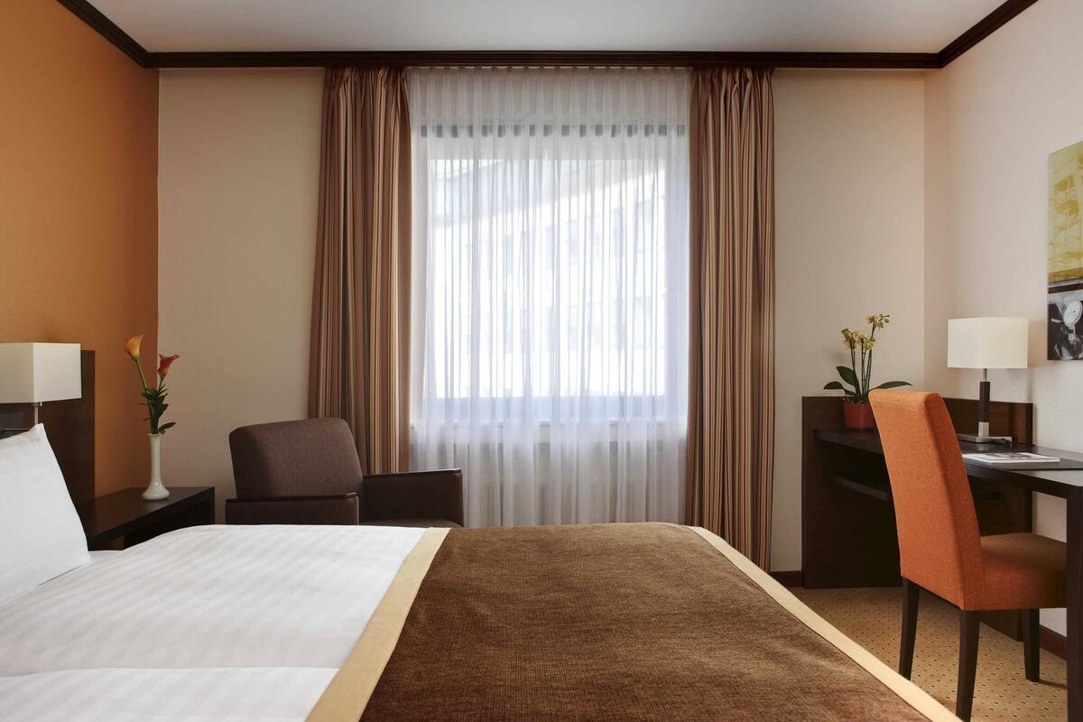 A hotel room with a bed, a desk, a chair, and a window with curtains.