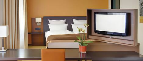 A hotel room with a bed, a desk, a television, and a potted plant.