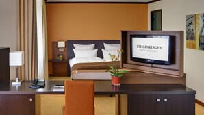 A hotel room with a bed, a desk with a telephone, a TV mounted on the wall, and a potted plant. - Steigenberger Hotel Dortmund (Dortmund)