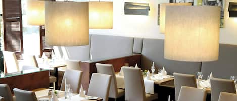 Interior de restaurante con mesas dispuestas para comer, sillas y lámparas colgantes.