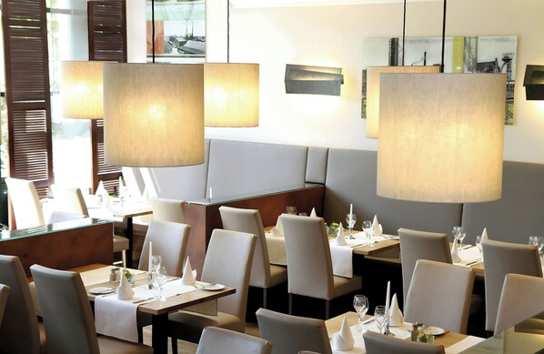 Interior de restaurante con mesas dispuestas para comer, sillas y lámparas colgantes.