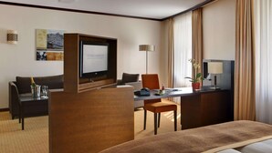 A hotel room with a bed, a desk with a computer, a chair, a television, a lamp, and a window with curtains. - Leonardo Royal Hotel Dortmund (Dortmund)