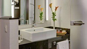 A modern bathroom with a white sink, a mirror, and a vase with flowers. - Leonardo Royal Hotel Dortmund (Dortmund)