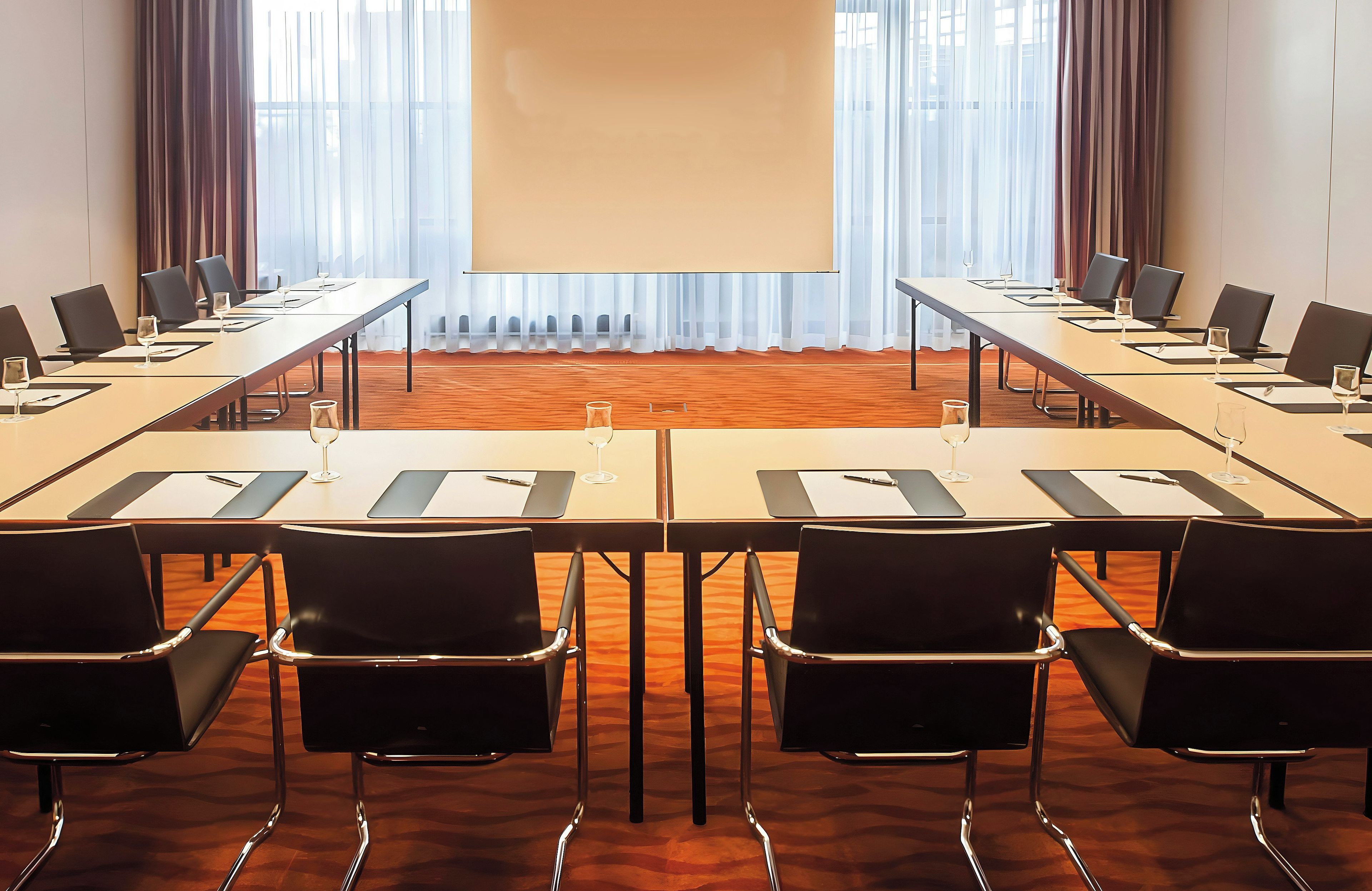 Un salón de conferencias con una mesa larga, sillas y una pantalla para presentaciones.