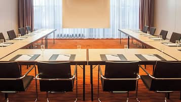 Un salón de conferencias con una mesa larga, sillas y una pantalla para presentaciones.